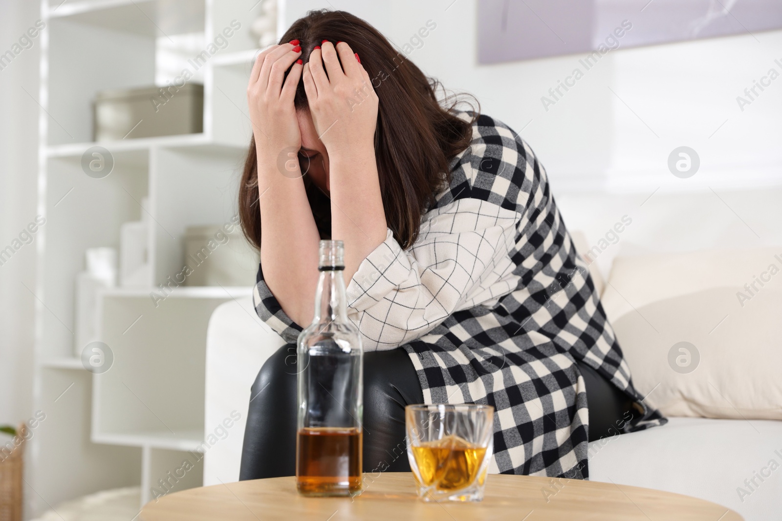 Photo of Alcohol addiction. Woman near wooden table with glass of whiskey and bottle at home