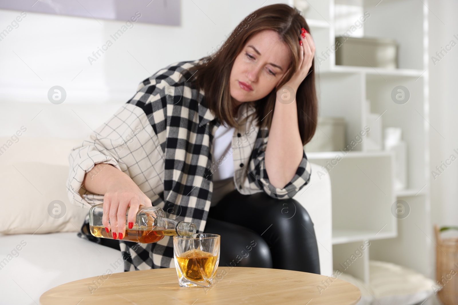 Photo of Alcohol addiction. Woman pouring whiskey into glass at table indoors