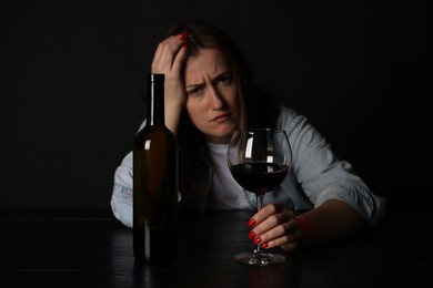 Photo of Alcohol addiction. Miserable woman with wine at table in dark