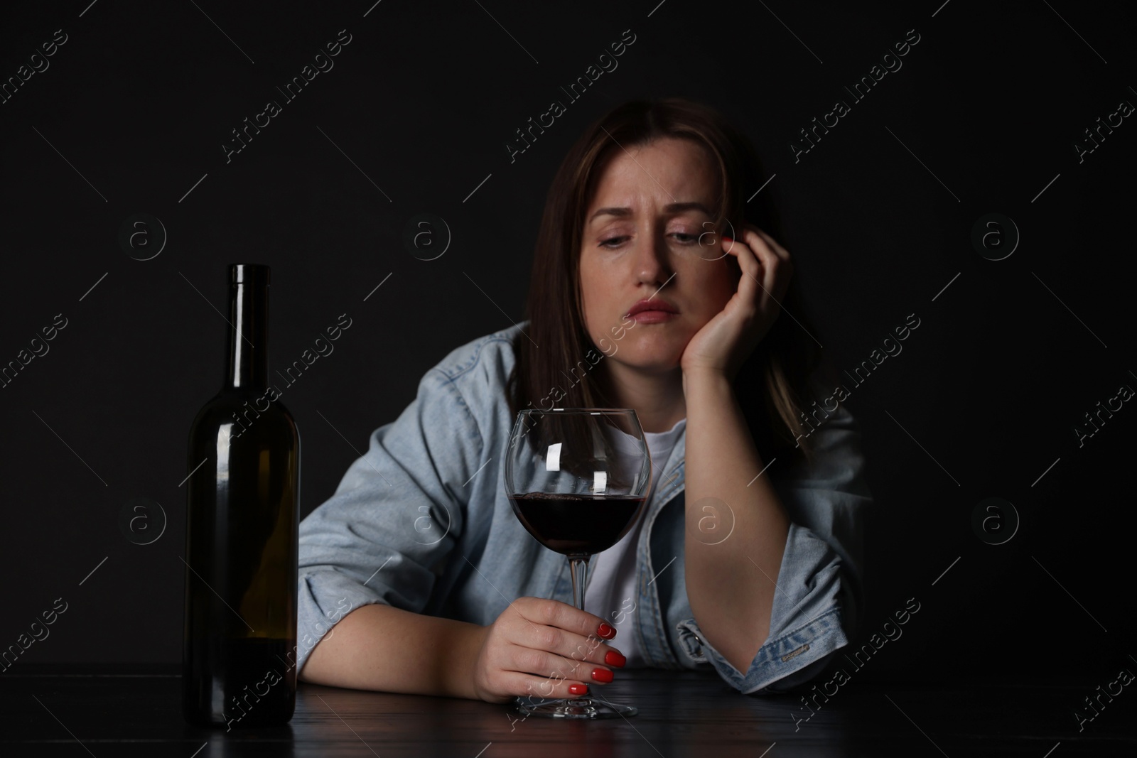 Photo of Alcohol addiction. Miserable woman with wine at table in dark