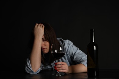 Photo of Alcohol addiction. Miserable woman with wine at table in dark