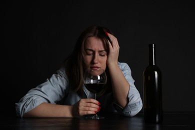 Photo of Alcohol addiction. Miserable woman with wine at table in dark