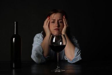 Photo of Alcohol addiction. Miserable woman with wine at table in dark, selective focus