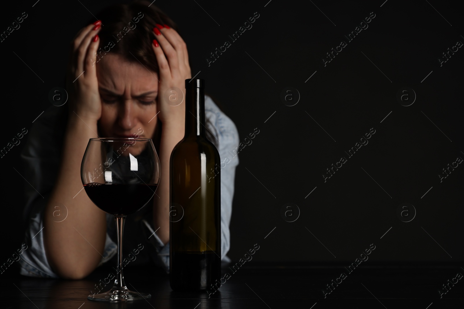 Photo of Alcohol addiction. Miserable woman with wine at table in dark. Space for text