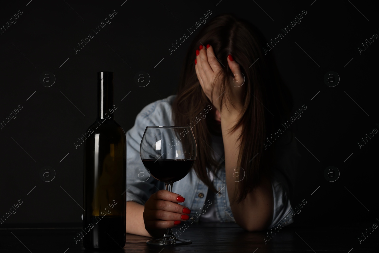 Photo of Alcohol addiction. Miserable woman with wine at table in dark