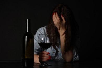 Photo of Alcohol addiction. Miserable woman with wine at table in dark