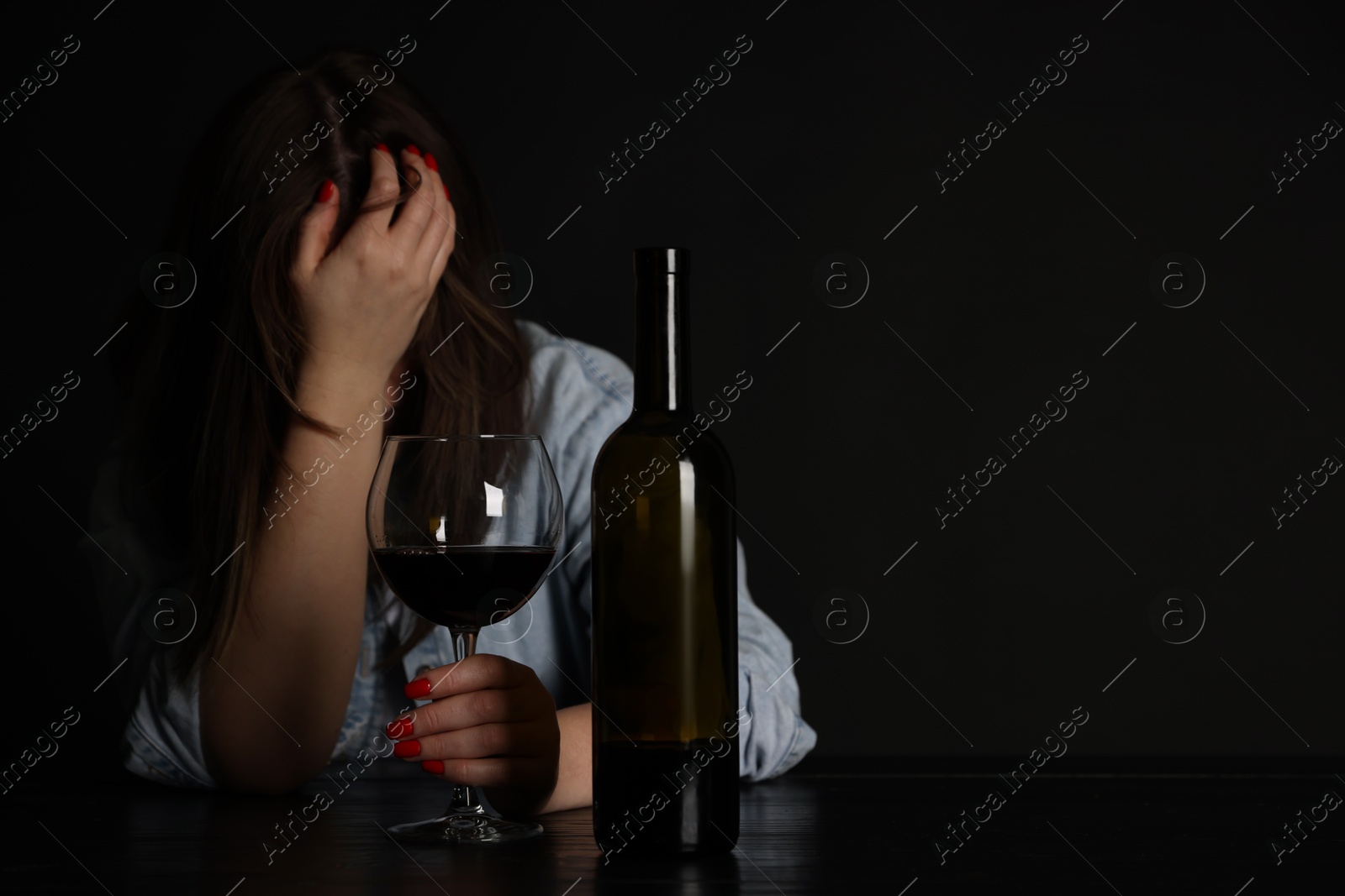 Photo of Alcohol addiction. Miserable woman with wine at table in dark. Space for text