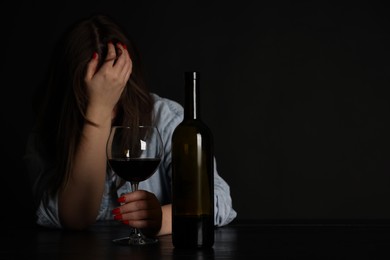 Photo of Alcohol addiction. Miserable woman with wine at table in dark. Space for text