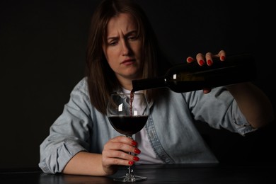 Photo of Alcohol addiction. Miserable woman pouring wine into glass at table in dark