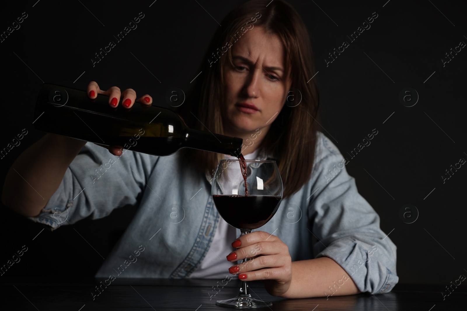 Photo of Alcohol addiction. Miserable woman pouring wine into glass at table in dark