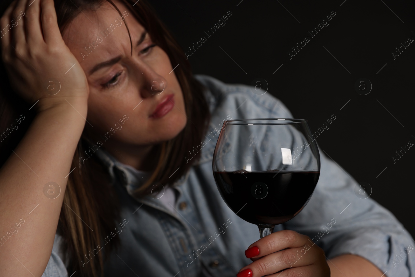 Photo of Alcohol addiction. Miserable woman with wine in dark