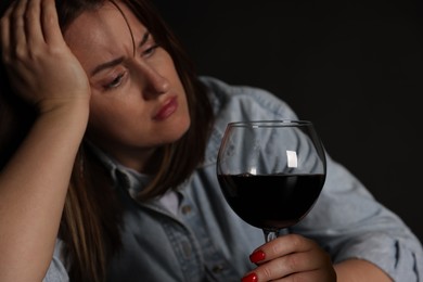 Photo of Alcohol addiction. Miserable woman with wine in dark