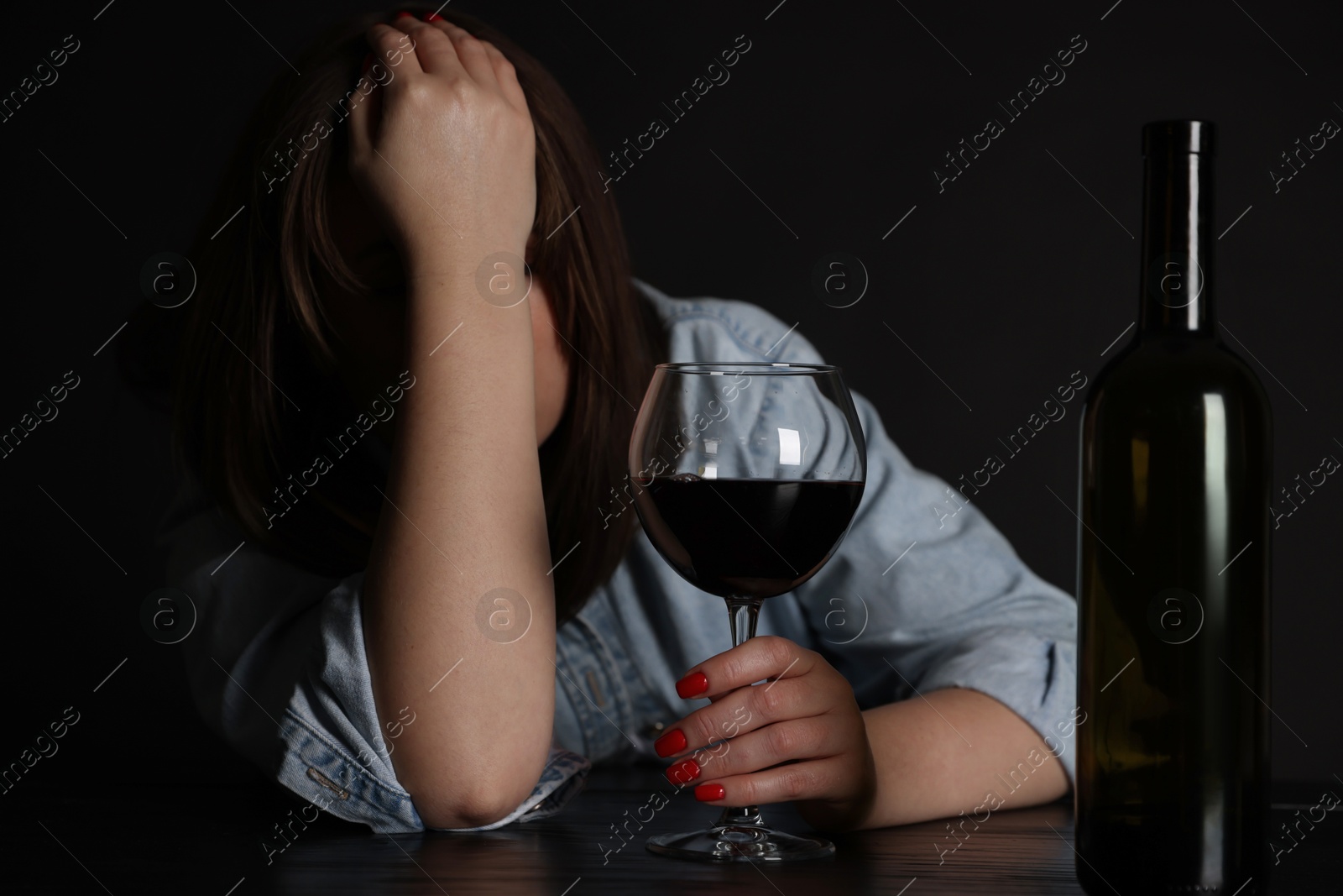 Photo of Alcohol addiction. Miserable woman with wine at table in dark