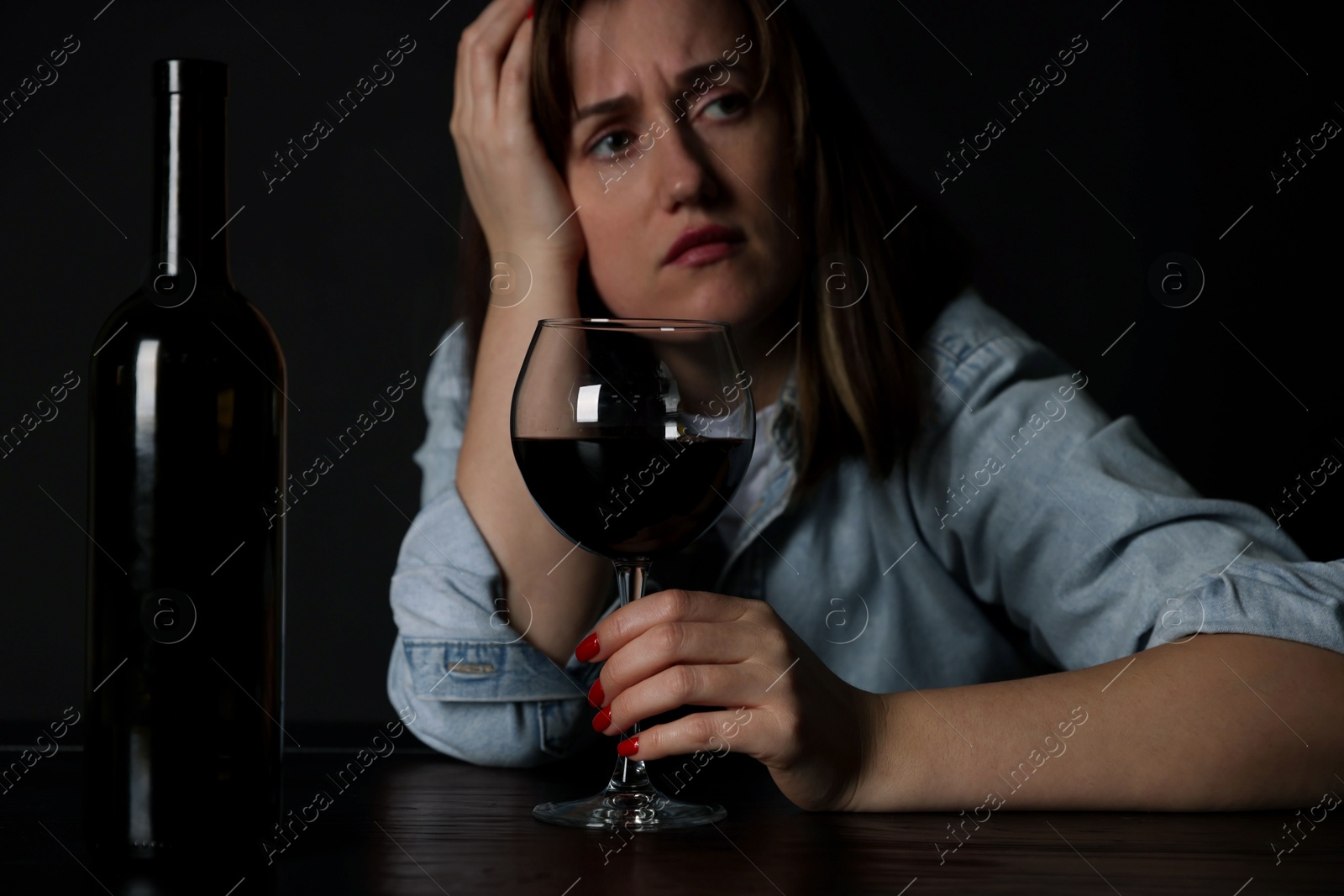 Photo of Alcohol addiction. Miserable woman with wine at table in dark