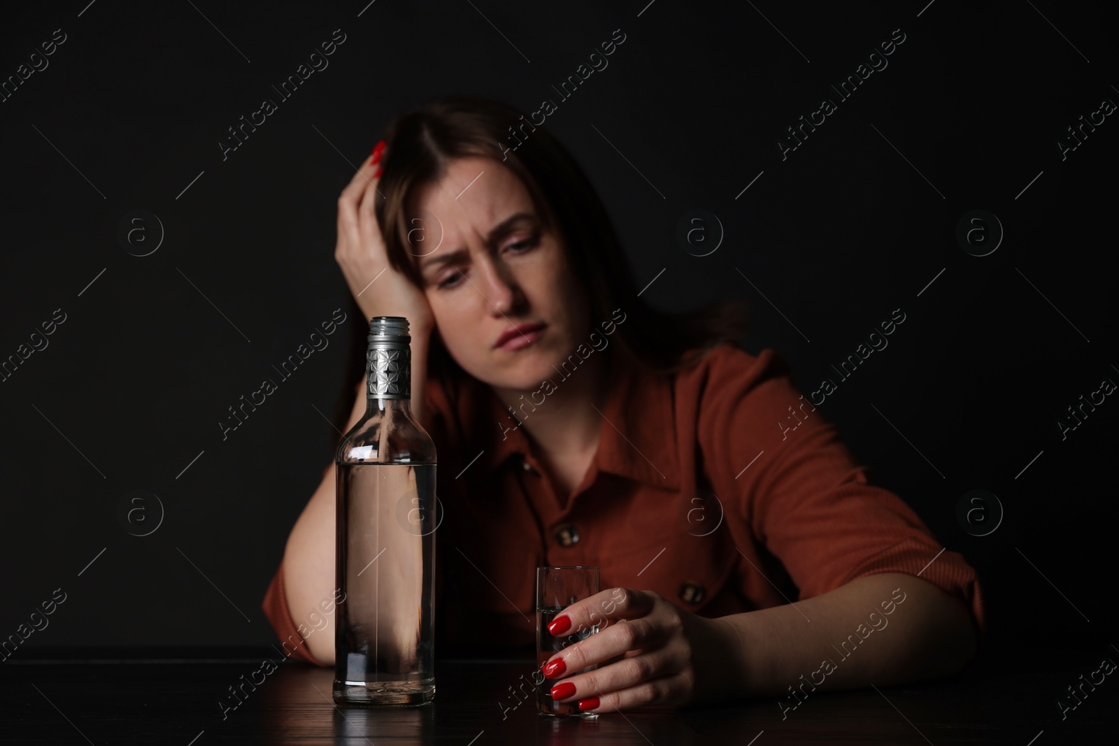 Photo of Alcohol addiction. Miserable woman with vodka at table in dark