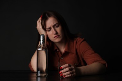 Photo of Alcohol addiction. Miserable woman with vodka at table in dark