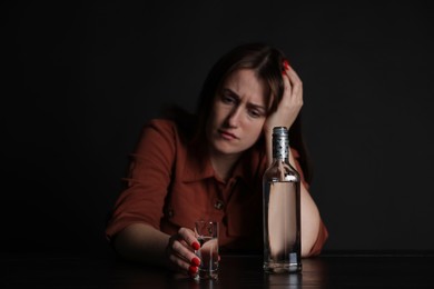 Photo of Alcohol addiction. Miserable woman with vodka at table in dark