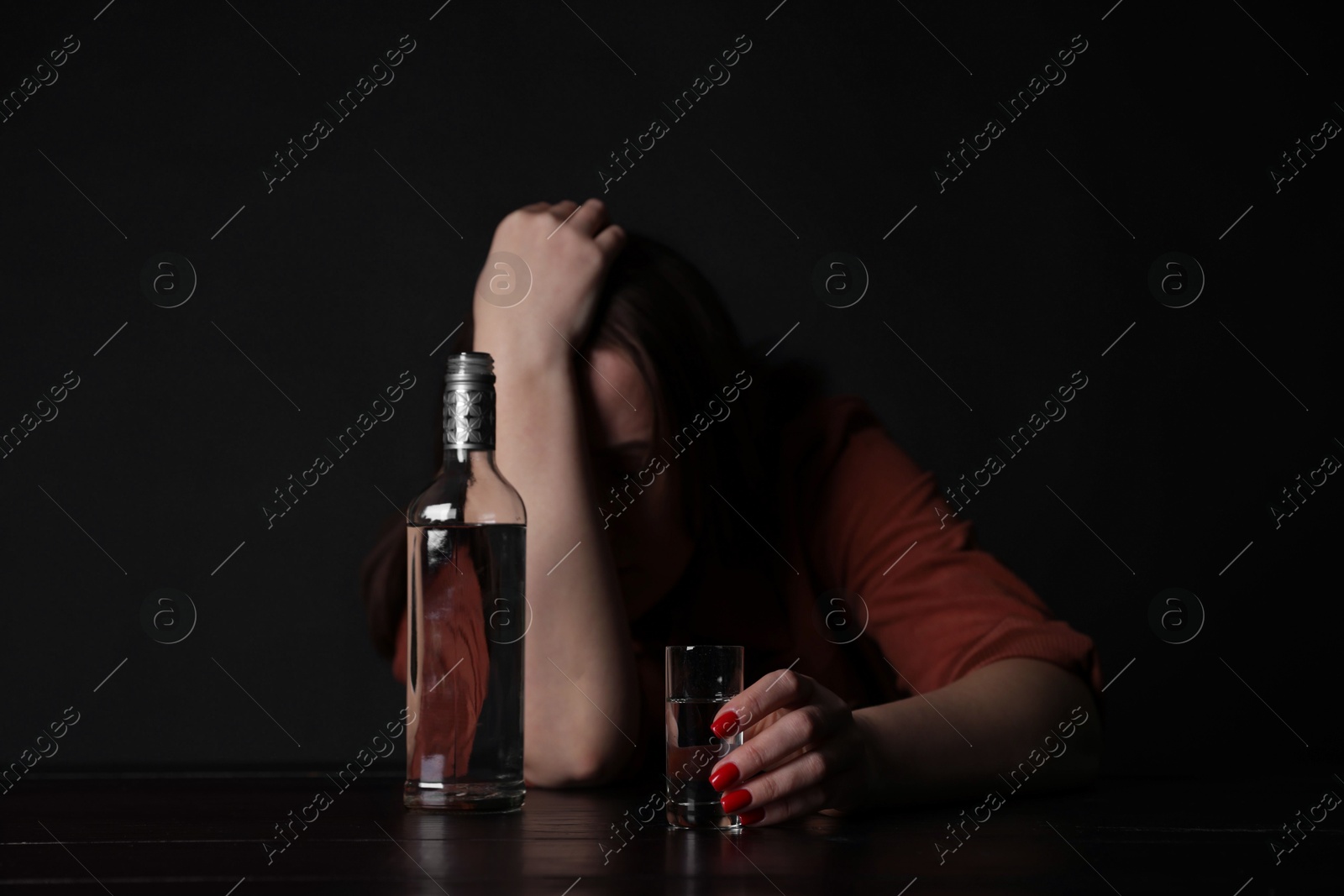 Photo of Alcohol addiction. Miserable woman with vodka at table in dark