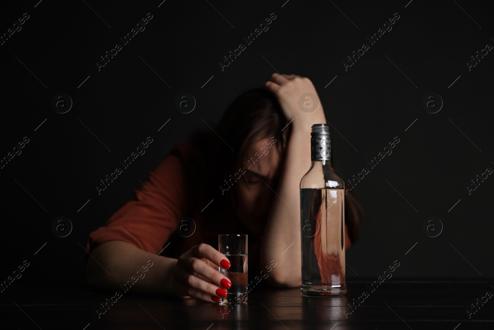 Photo of Alcohol addiction. Miserable woman with vodka at table in dark