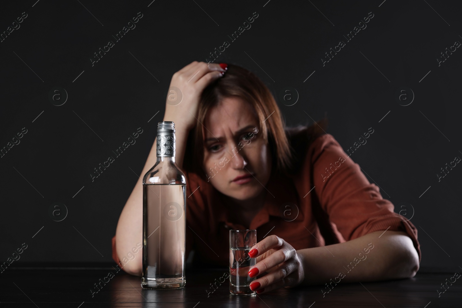 Photo of Alcohol addiction. Miserable woman with vodka at table in dark