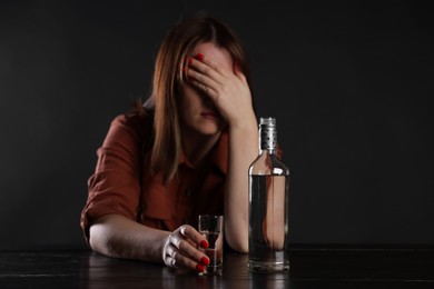 Photo of Alcohol addiction. Miserable woman with vodka at table in dark