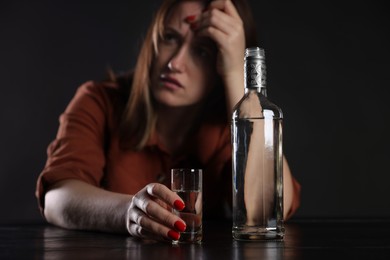 Photo of Alcohol addiction. Miserable woman with vodka at table in dark