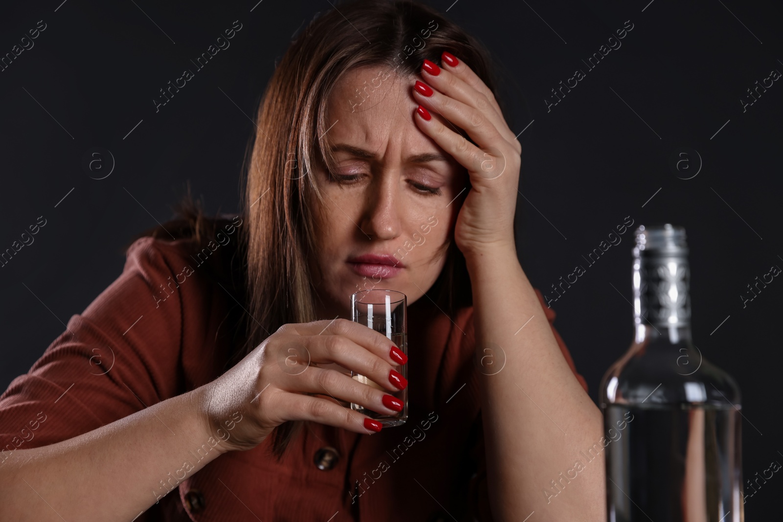 Photo of Alcohol addiction. Miserable woman drinking vodka in dark