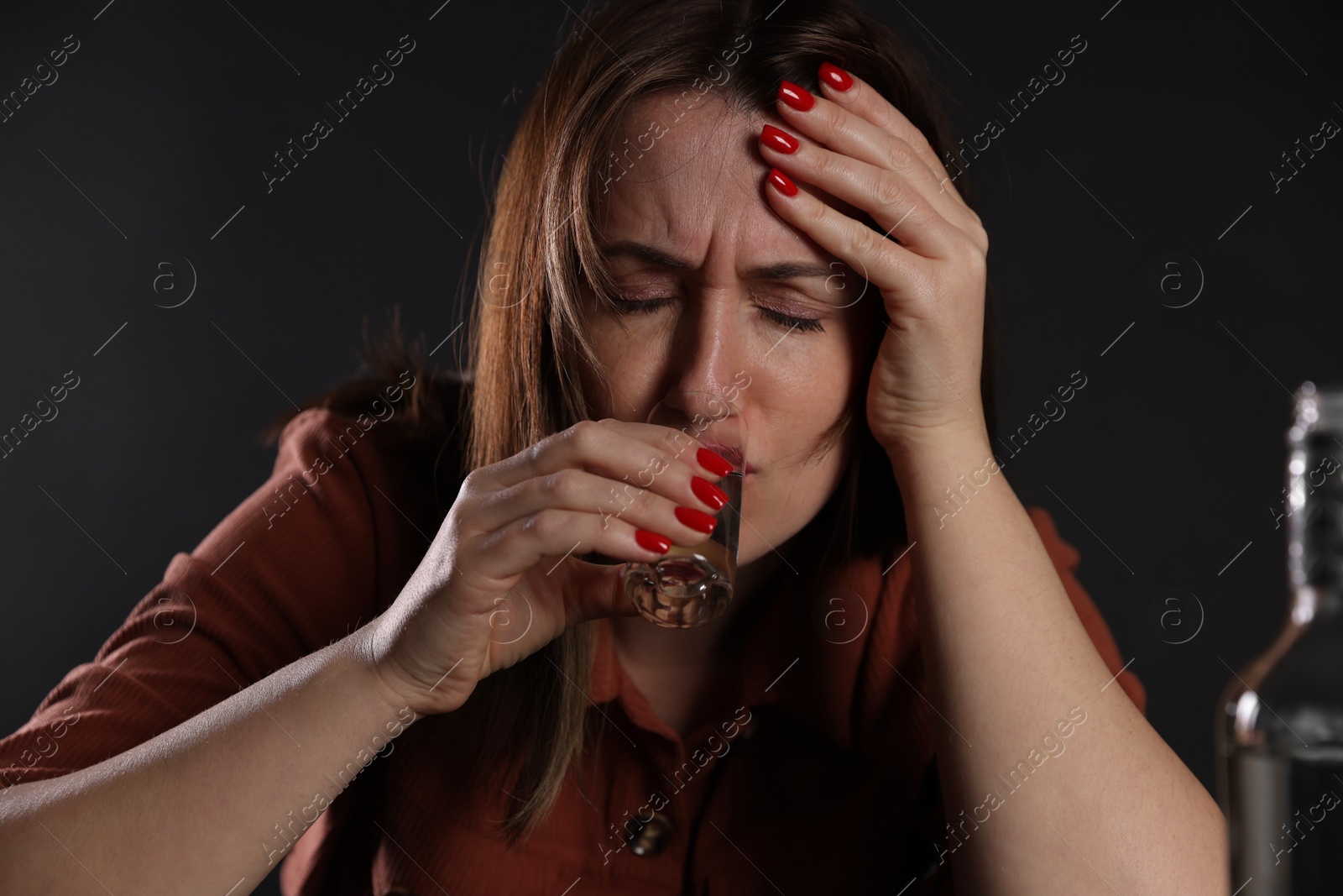 Photo of Alcohol addiction. Miserable woman drinking vodka in dark