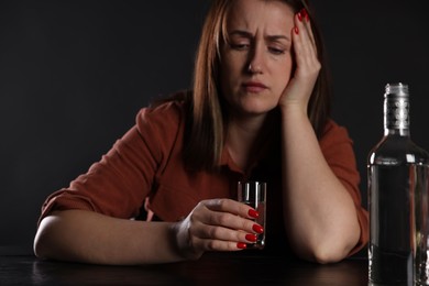 Photo of Alcohol addiction. Miserable woman with vodka at table in dark