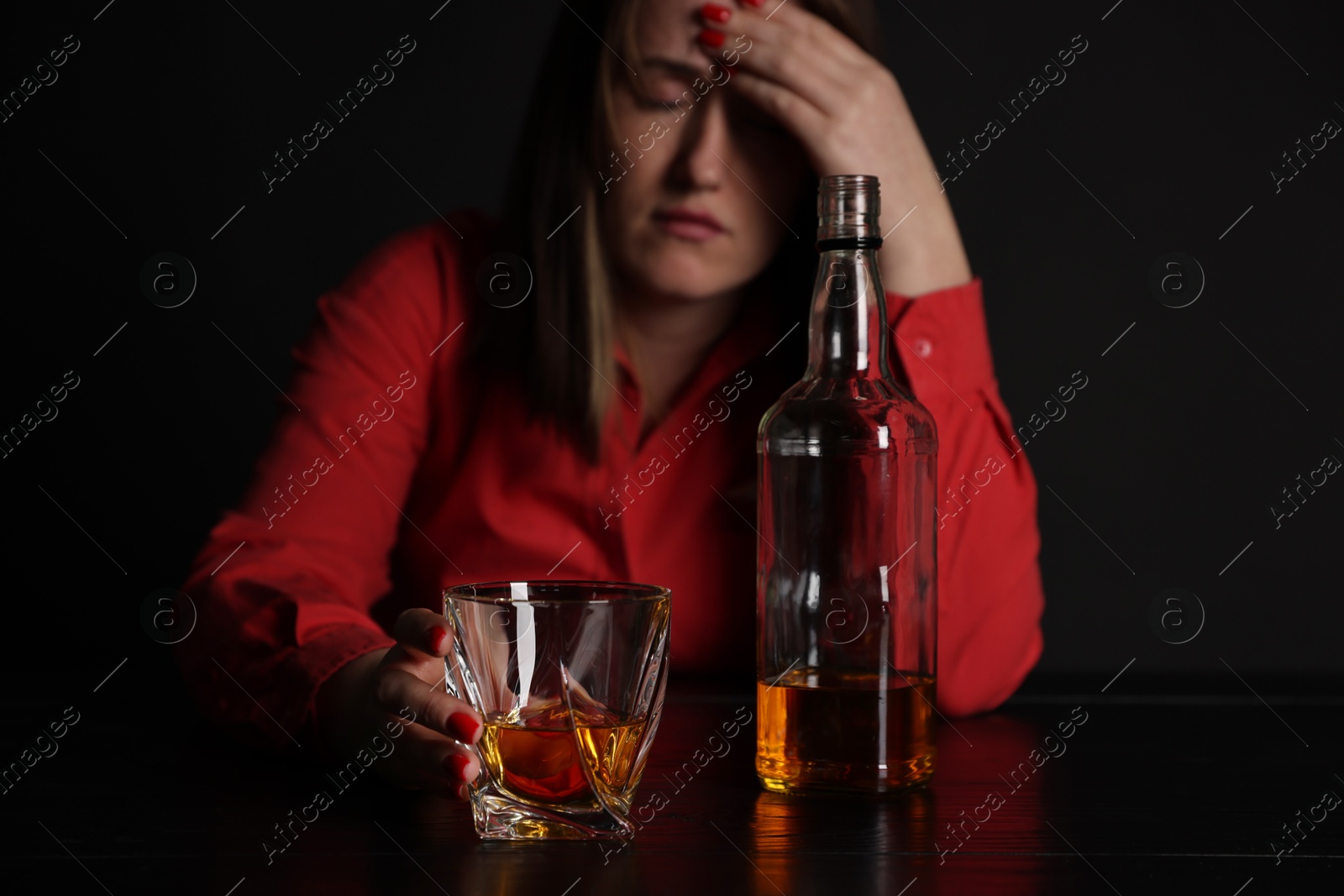 Photo of Alcohol addiction. Miserable woman with whiskey at table in dark, selective focus