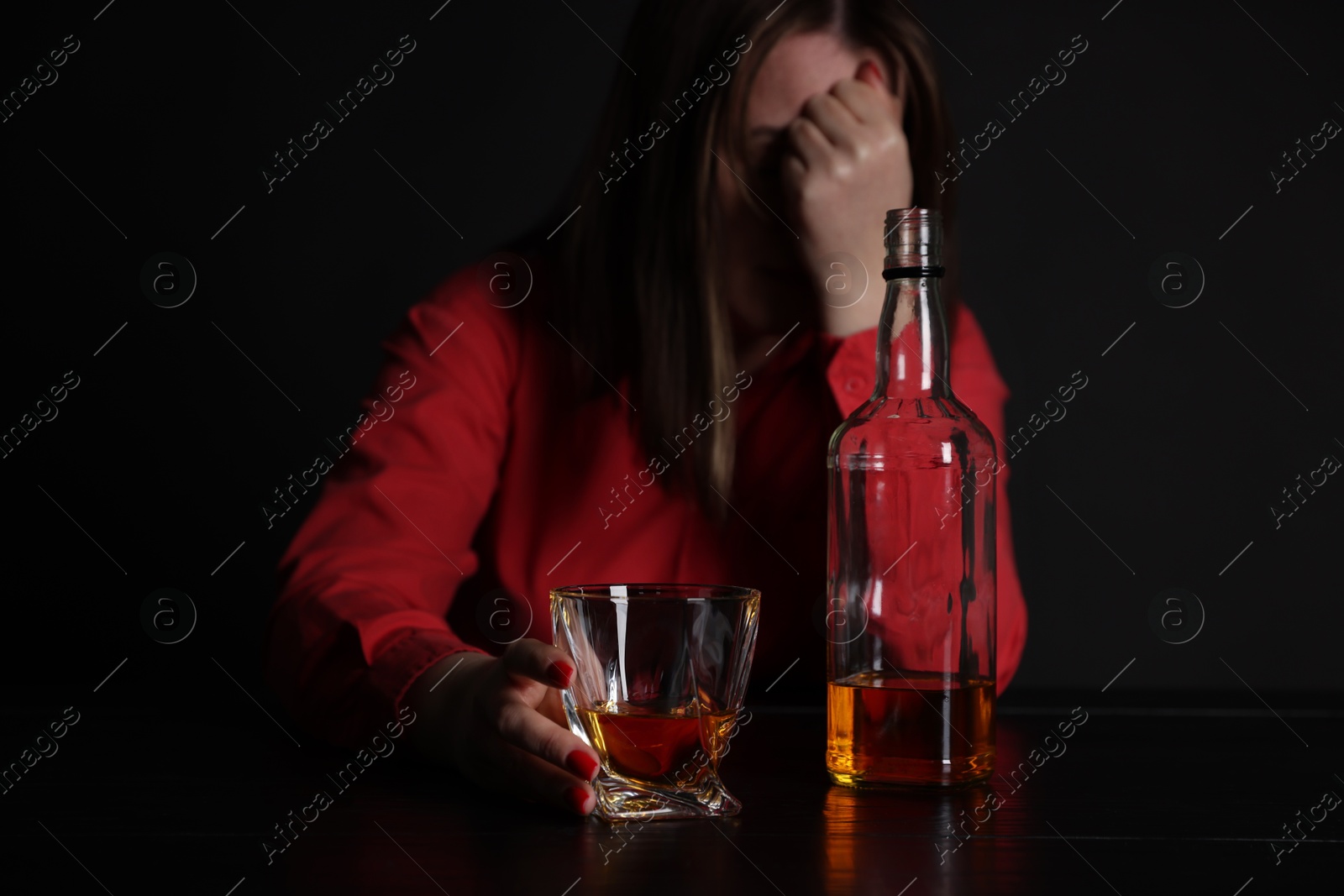 Photo of Alcohol addiction. Miserable woman with whiskey at table in dark