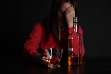 Photo of Alcohol addiction. Miserable woman with whiskey at table in dark