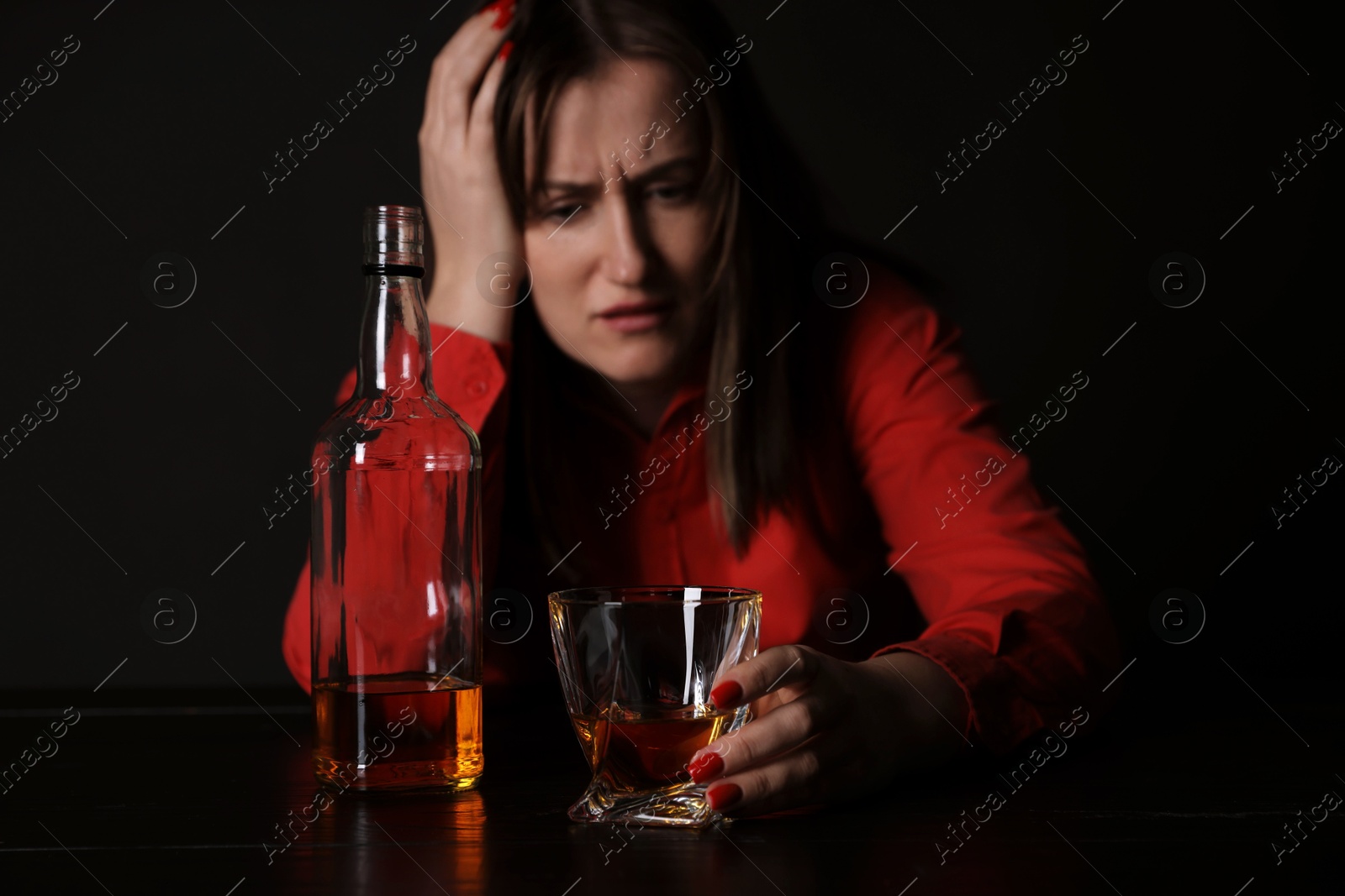 Photo of Alcohol addiction. Miserable woman with whiskey at table in dark