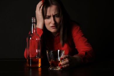 Photo of Alcohol addiction. Miserable woman with whiskey at table in dark