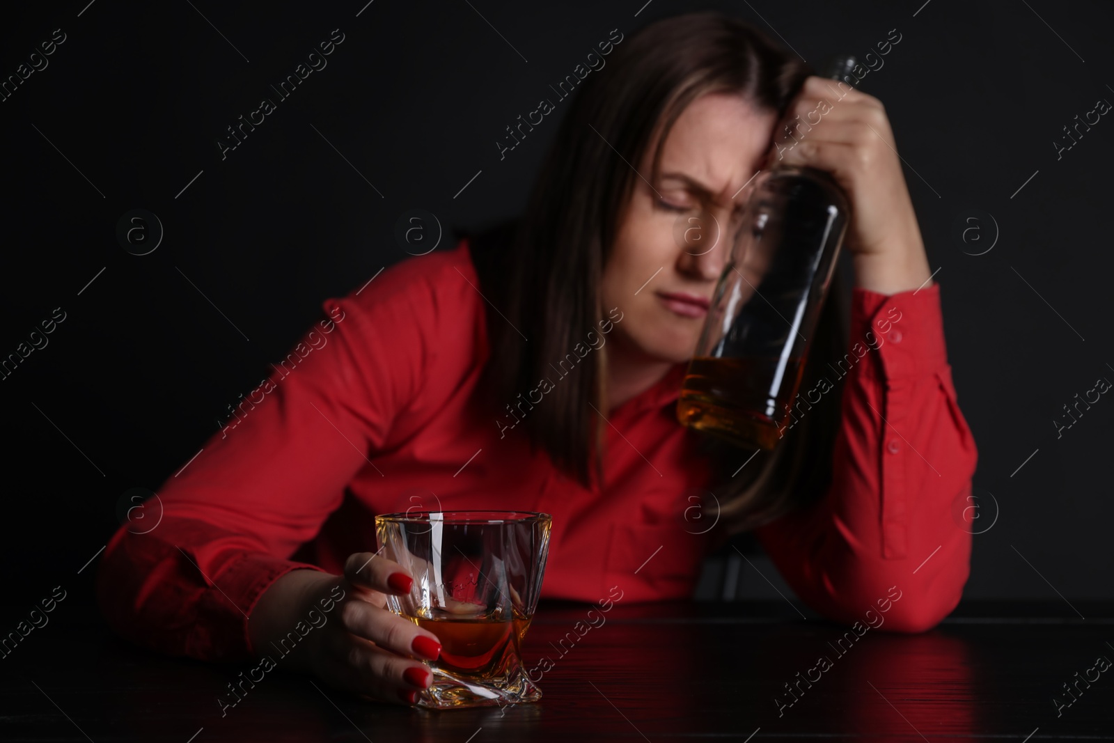 Photo of Alcohol addiction. Miserable woman with whiskey at table in dark