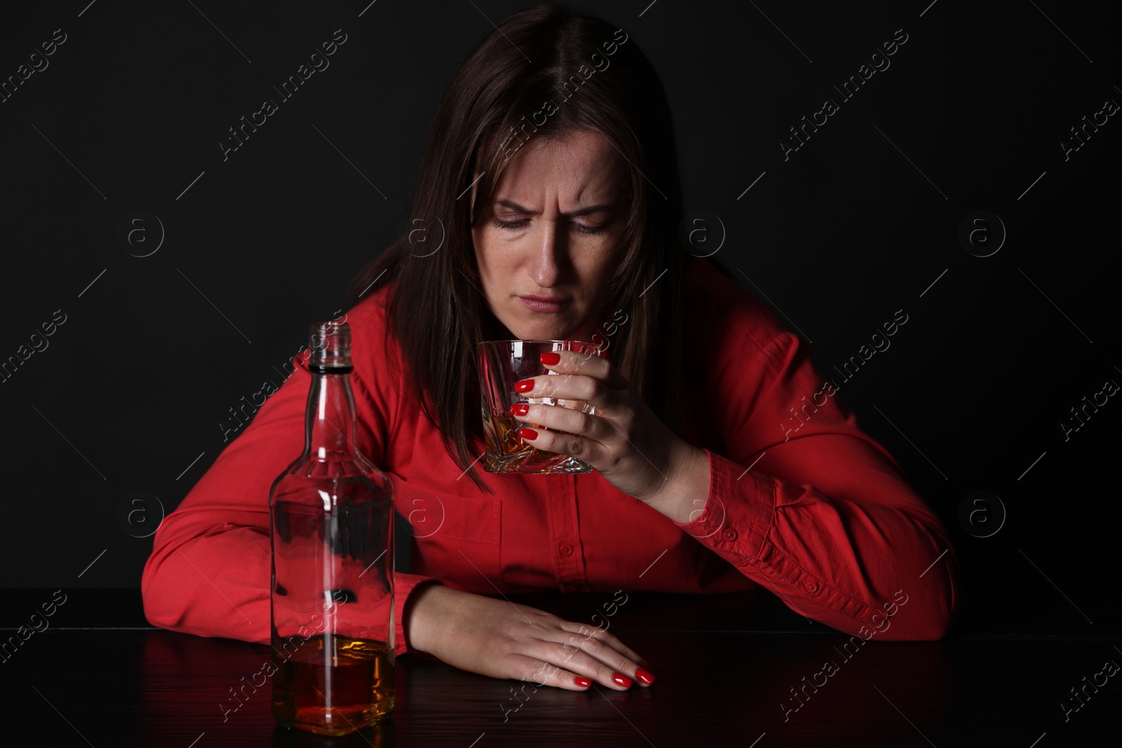 Photo of Alcohol addiction. Miserable woman drinking whiskey at table in dark