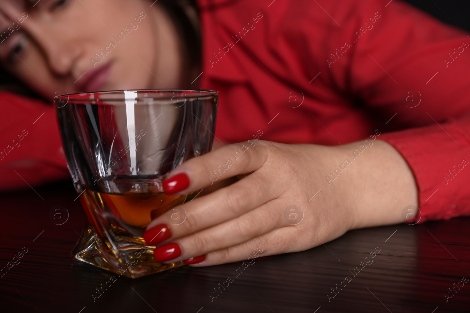 Photo of Alcohol addiction. Miserable woman with whiskey at table in dark, selective focus