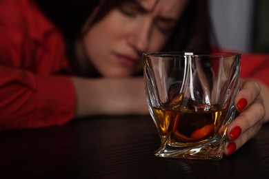 Photo of Alcohol addiction. Miserable woman with whiskey at table in dark, selective focus