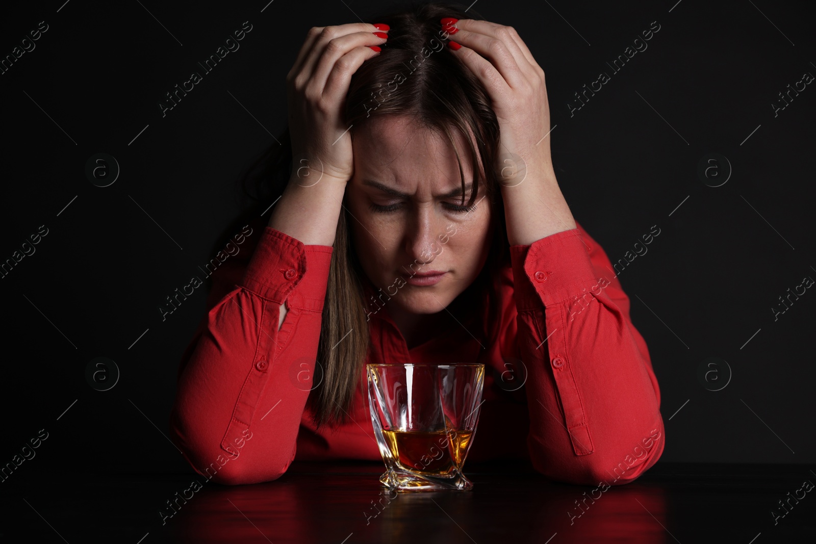 Photo of Alcohol addiction. Miserable woman with whiskey at table in dark