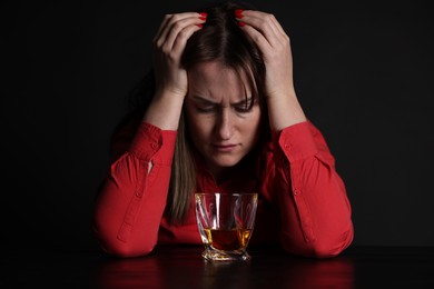 Photo of Alcohol addiction. Miserable woman with whiskey at table in dark