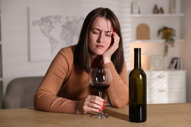 Photo of Alcohol addiction. Miserable woman with wine at table indoors