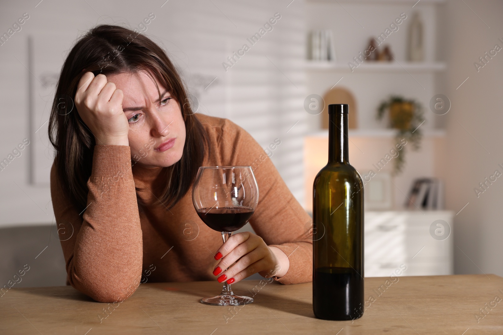 Photo of Alcohol addiction. Miserable woman with wine at table indoors