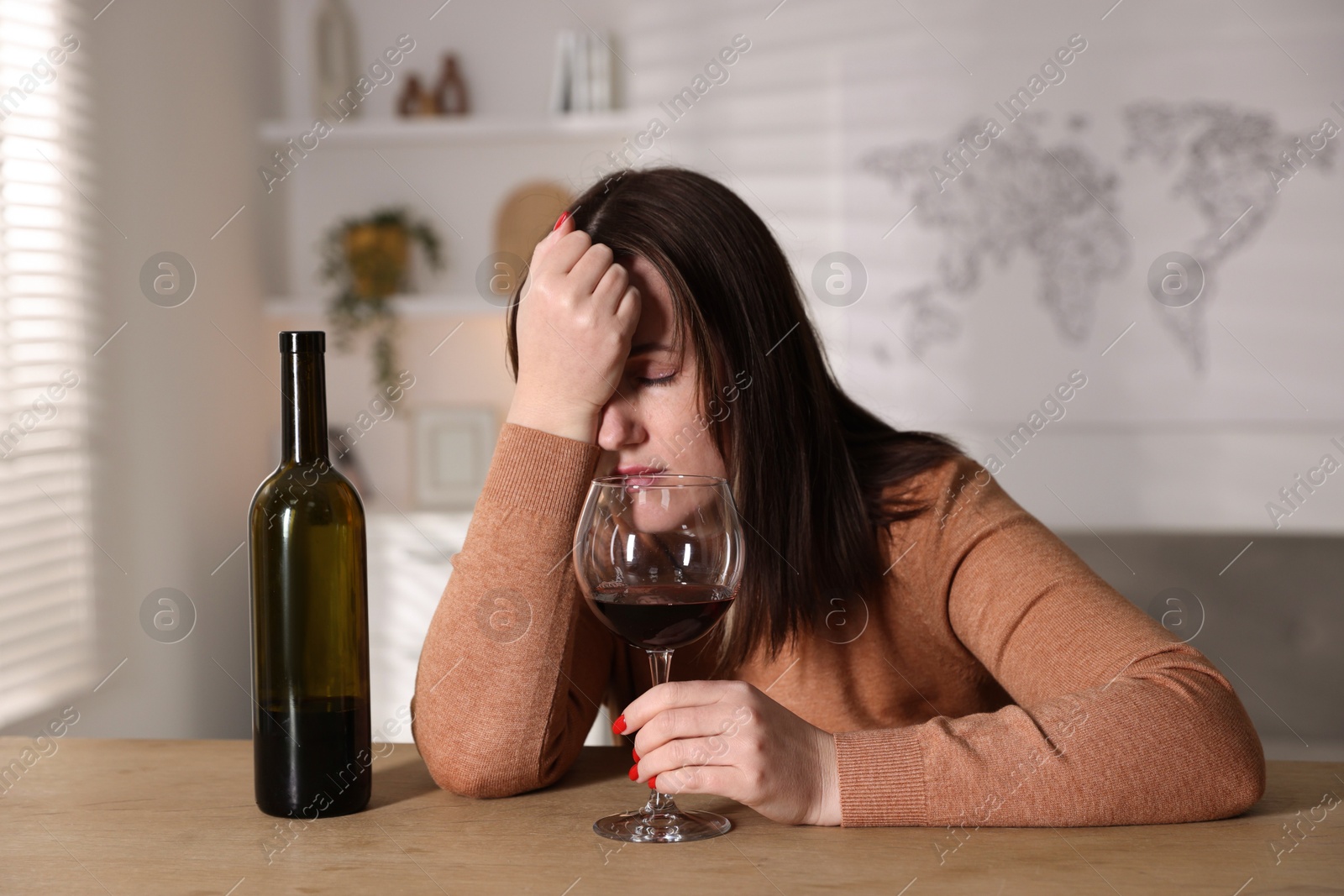 Photo of Alcohol addiction. Miserable woman with wine at table indoors