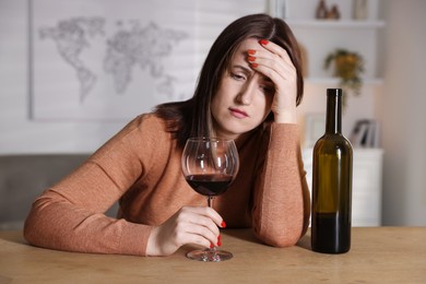 Photo of Alcohol addiction. Miserable woman with wine at table indoors