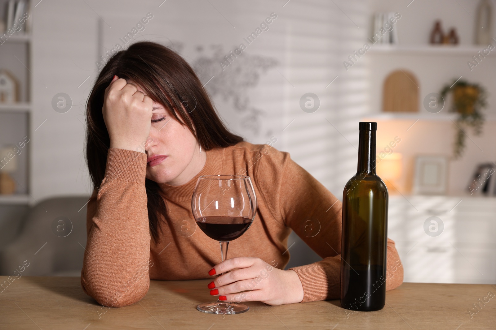 Photo of Alcohol addiction. Miserable woman with wine at table indoors