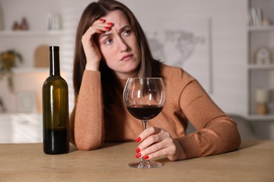 Photo of Alcohol addiction. Miserable woman with wine at table indoors