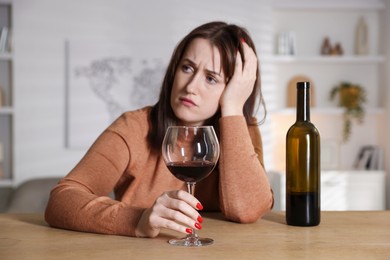 Photo of Alcohol addiction. Miserable woman with wine at table indoors