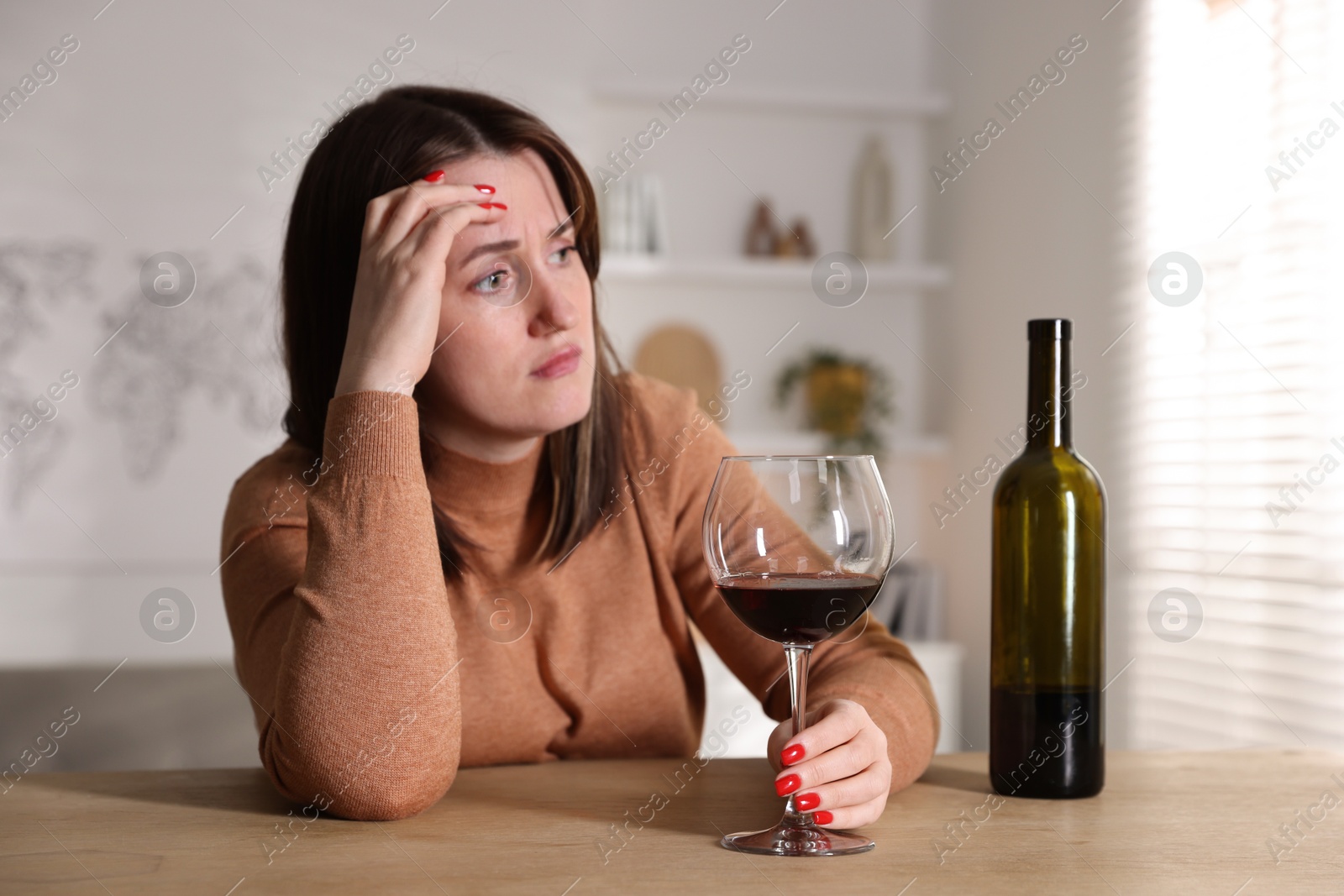 Photo of Alcohol addiction. Miserable woman with wine at table indoors