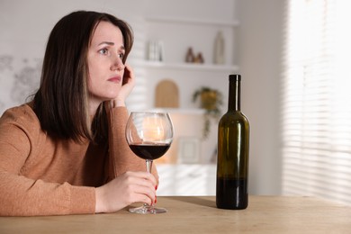 Photo of Alcohol addiction. Miserable woman with wine at table indoors