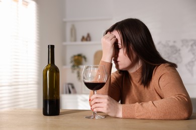 Photo of Alcohol addiction. Miserable woman with wine at table indoors